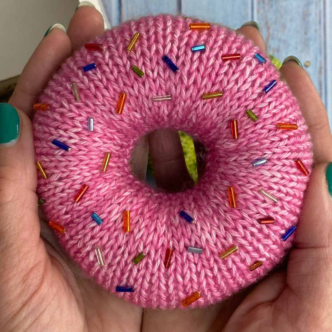 Knitted donut in pink with colourful sprinkles, made from free knitted donut pattern